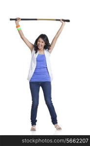 Full length portrait of happy young woman in casuals holding up hockey stick over white background