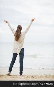 Full length portrait of happy young woman in sweater rejoicing on beach . rear view