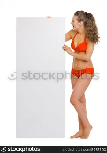 Full length portrait of happy young woman in swimsuit looking on blank billboard