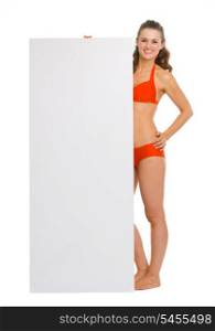 Full length portrait of happy young woman in swimsuit showing blank billboard
