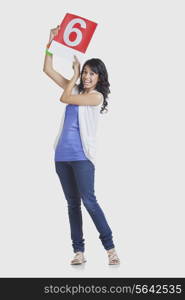 Full length portrait of happy young woman pointing at number 6 over white background