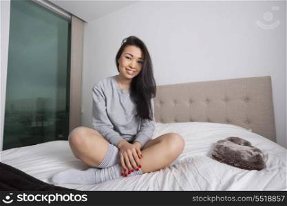 Full length portrait of happy young woman sitting on bed