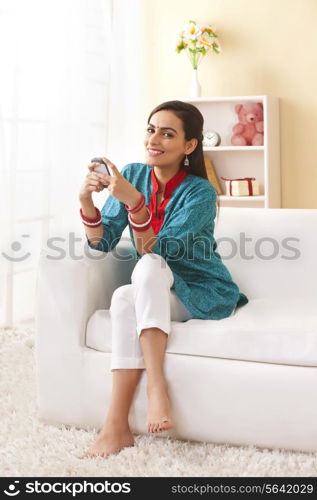 Full length portrait of happy young woman using mobile phone on sofa