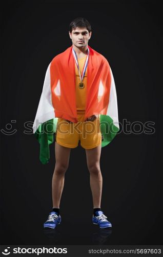 Full length portrait of male medalist with Indian flag standing against black background