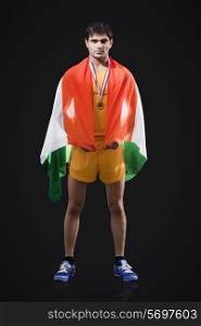 Full length portrait of male medalist with Indian flag standing against black background