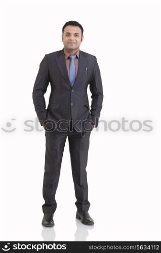 Full length portrait of mid adult businessman with hands in pockets against white background
