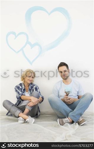 Full-length portrait of mid-adult couple with painted hearts on wall