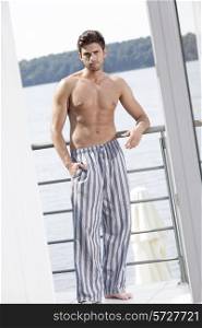 Full length portrait of muscular young man in pajama leaning on railing of hotel balcony