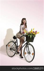 full-length portrait of sensual brunette pin-up girl on bicycle with vintage hair-style, pink shirt and short skirt. Some colourful tulips in bike s basket