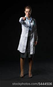 Full length portrait of serious doctor woman pointing in camera isolated on black