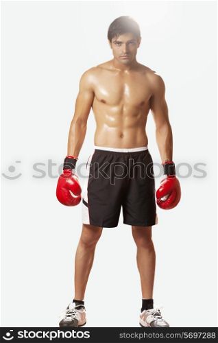 Full length portrait of shirtless young man wearing boxing gloves against white background
