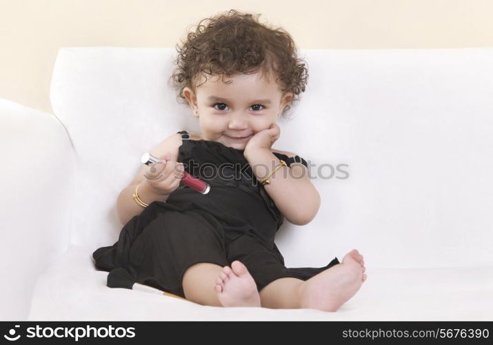 Full length portrait of smiling cute girl holding lip gloss on sofa
