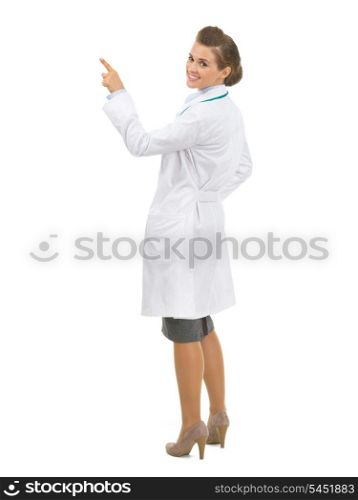 Full length portrait of smiling doctor woman pointing up on copy space