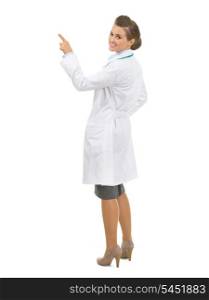 Full length portrait of smiling doctor woman pointing up on copy space