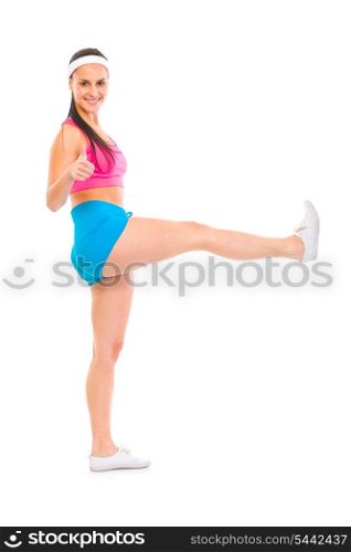Full length portrait of smiling fitness girl with raised leg showing thumbs up isolated on white&#xA;