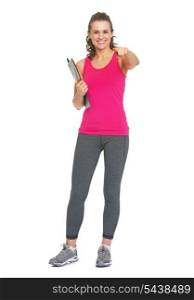 Full length portrait of smiling fitness trainer with clipboard pointing in camera