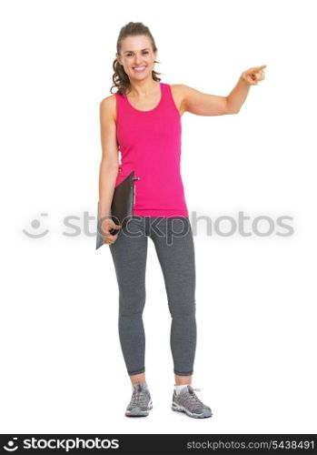Full length portrait of smiling fitness trainer with clipboard pointing on copy space