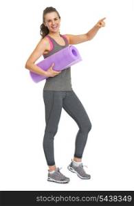 Full length portrait of smiling fitness young woman with fitness mat pointing on copy space