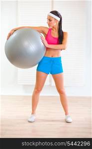 Full length portrait of smiling healthy girl holding fitness ball at living room&#xA;
