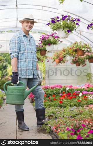Full-length portrait of smiling man carrying watering can in greenhouse
