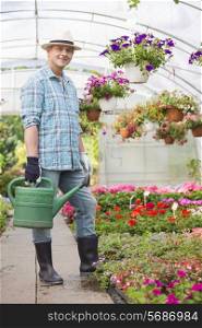Full-length portrait of smiling man carrying watering can in greenhouse