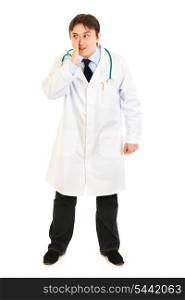 Full length portrait of smiling medical doctor holding his hand near mouth and secretly reporting good news isolated on white&#xA;