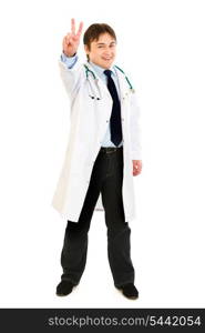 Full length portrait of smiling medical doctor showing victory gesture isolated on white&#xA;