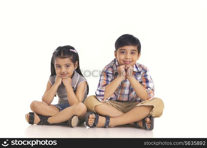 Full length portrait of smiling siblings sitting over white background