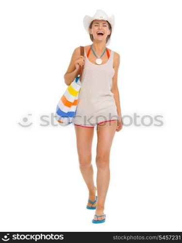 Full length portrait of smiling young beach woman in hat going straight