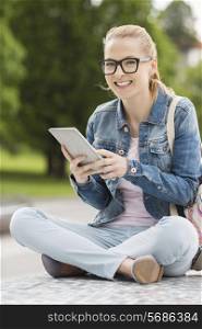 Full length portrait of smiling young female college student using tablet PC in park