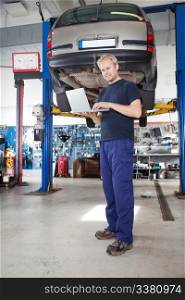 Full length portrait of smiling young mechanic using laptop in his auto repair shop