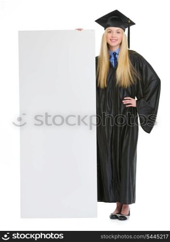 Full length portrait of smiling young woman in graduation gown showing blank billboard