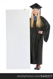 Full length portrait of smiling young woman in graduation gown showing blank billboard