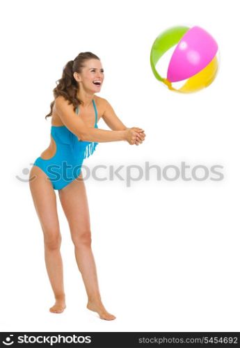 Full length portrait of smiling young woman in swimsuit playing with beach ball