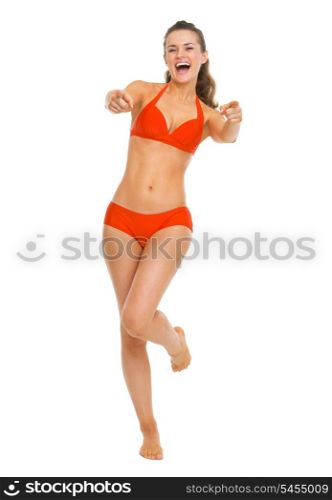 Full length portrait of smiling young woman in swimsuit pointing in camera