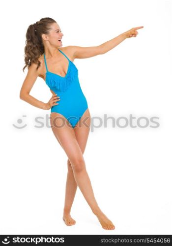Full length portrait of smiling young woman in swimsuit pointing on copy space