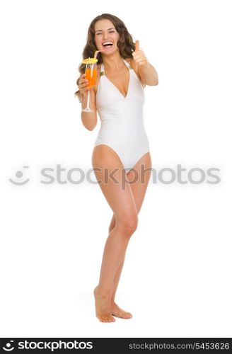 Full length portrait of smiling young woman in swimsuit with cocktail showing thumbs up
