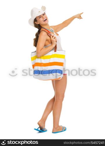 Full length portrait of smiling young woman with beach bag pointing on copy space