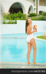 Full length portrait of smiling young woman with cocktail at poolside