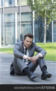 Full length portrait of stressed businessman sitting on path outside office
