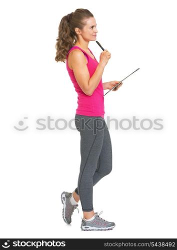 Full length portrait of thoughtful fitness trainer with clipboard looking on copy space