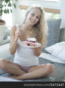 Full length portrait of woman having raspberry cake on sofa