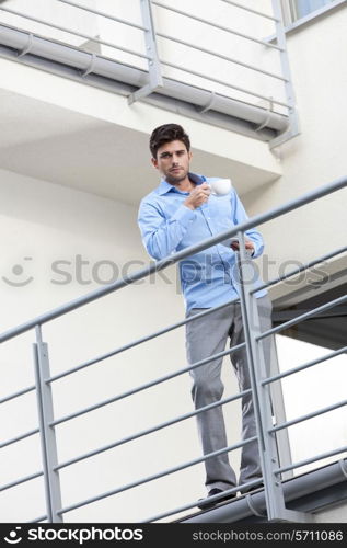 Full length portrait of young businessman having coffee at hotel balcony