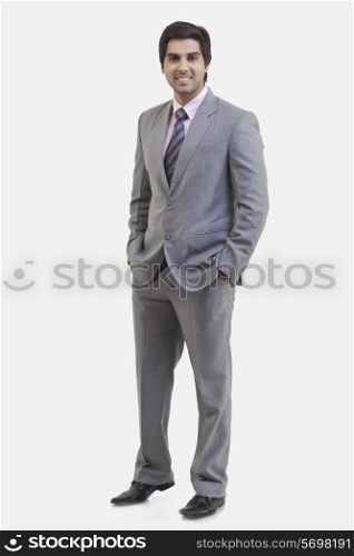 Full length portrait of young businessman with hands in pockets standing against white background