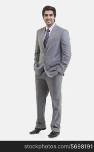 Full length portrait of young businessman with hands in pockets standing against white background