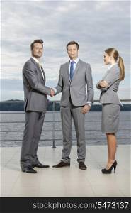 Full length portrait of young businessmen shaking hands while businesswoman looking at them on terrace