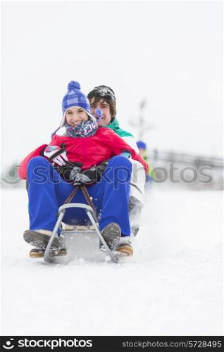 Full length portrait of young couple enjoying sled ride in snow