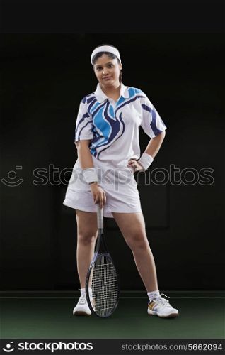 Full length portrait of young female player holding tennis racket against black background