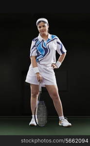 Full length portrait of young female player holding tennis racket against black background