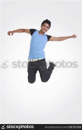 Full length portrait of young man jumping with arms outstretched over white background